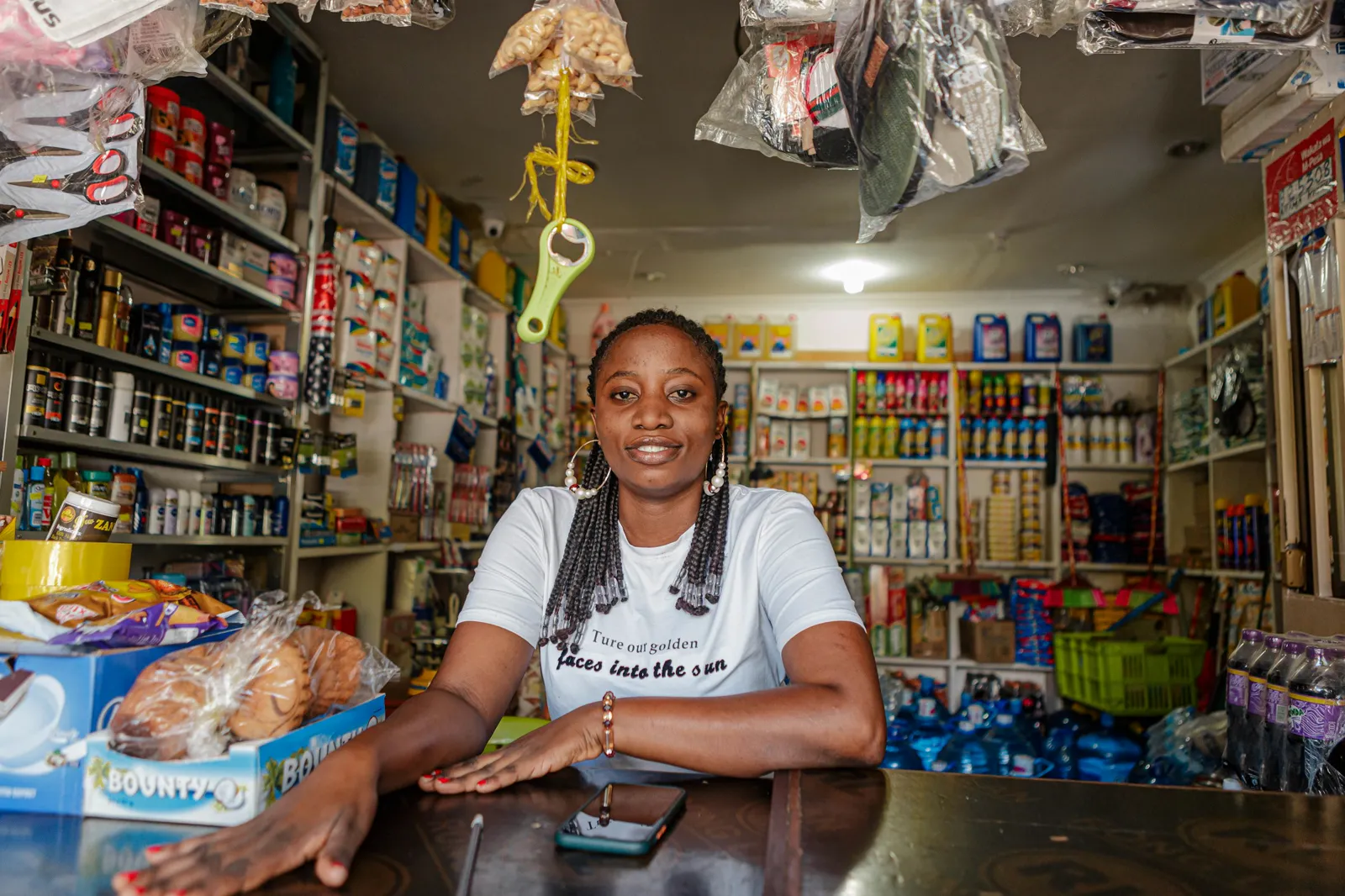A shop owner smiling at her counter, shelves of goods behind her
