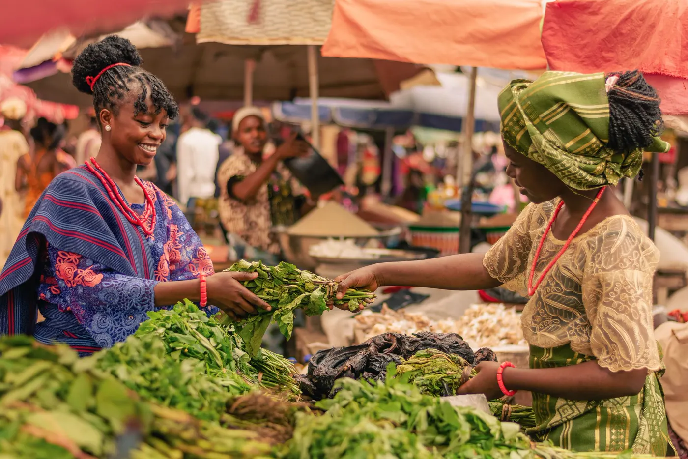A trader handing a bundle of vegetables to a customer across her market stall